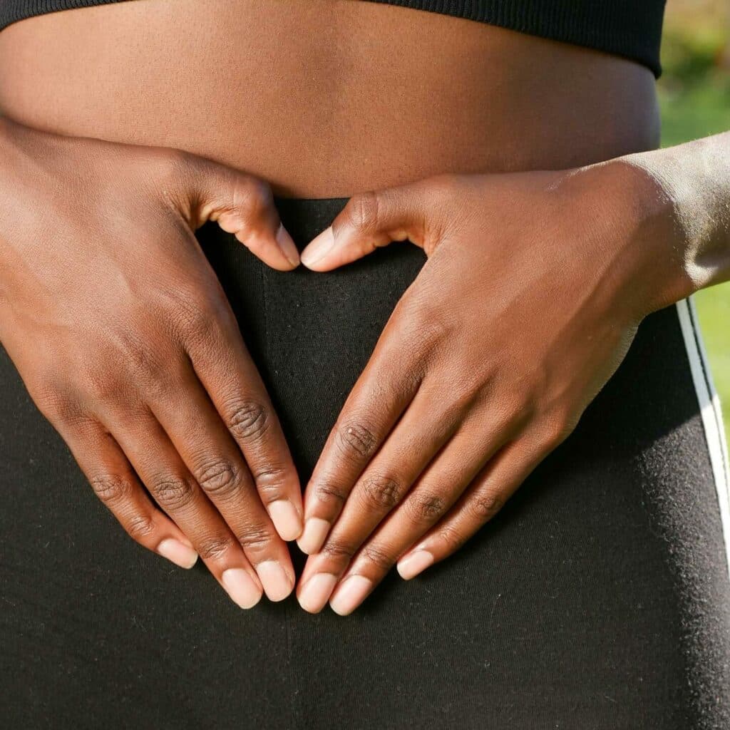 Close-up of hands forming a heart shape on woman's belly, symbolizing health and love.